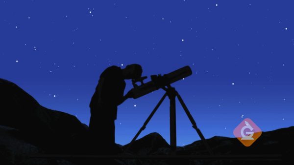 man looks at the night sky through a telescope